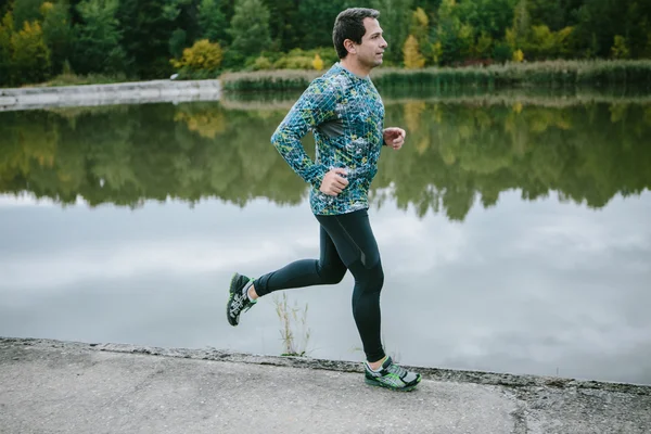 Man at the lake running against green cloudy nature — Stockfoto