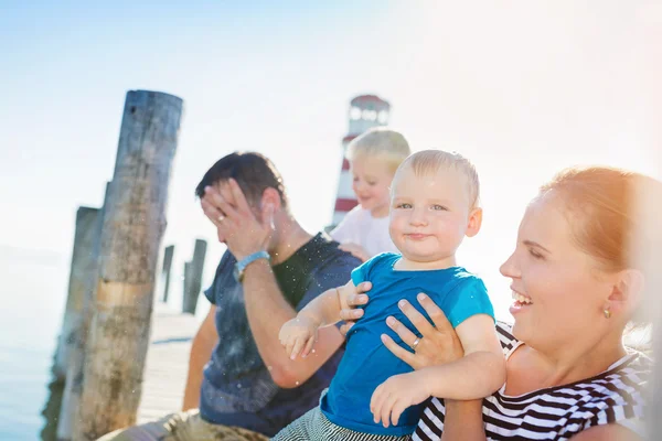 Family sitting on the pier, lighthouse, sunny summer day — Stock fotografie