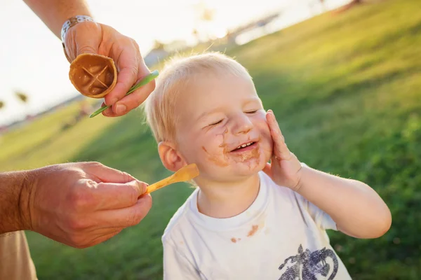 Boy eating ice cream, dirty face, green meadow, sunny — Zdjęcie stockowe