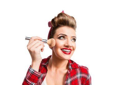 Woman with pin-up hairstyle applying make-up with a brush