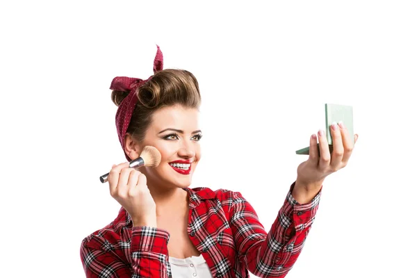 Woman, pin-up hairstyle holding mirror, applying make-up with br — Stok fotoğraf