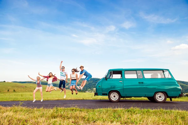 Jumping frieds with campervan, green nature and blue sky — Stock fotografie