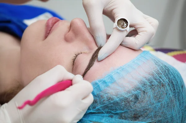 Cosmetólogo aplicando maquillaje permanente (tatuaje) en las cejas . —  Fotos de Stock