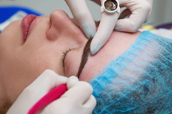 Cosmetólogo aplicando maquillaje permanente (tatuaje) en las cejas . —  Fotos de Stock