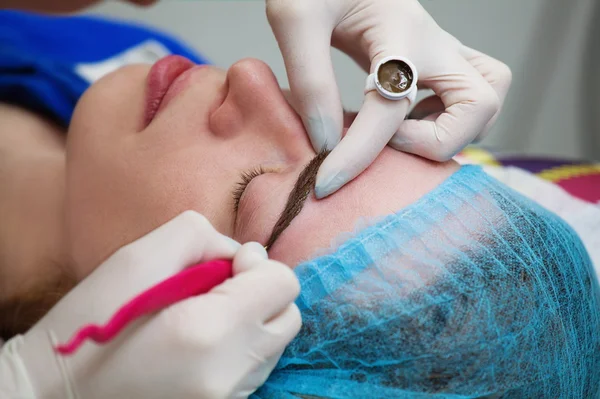 Cosmetologist que aplica a composição permanente (tatuagem) em sobrancelhas . Fotos De Bancos De Imagens Sem Royalties