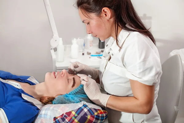 Cosmetologist que aplica a composição permanente (tatuagem) em sobrancelhas . — Fotografia de Stock