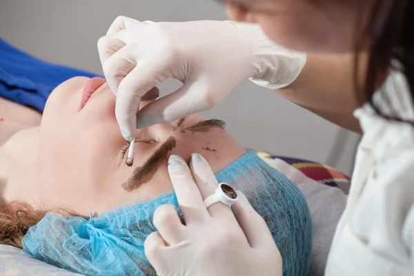 Cosmetologist que aplica a composição permanente (tatuagem) em sobrancelhas . — Fotografia de Stock