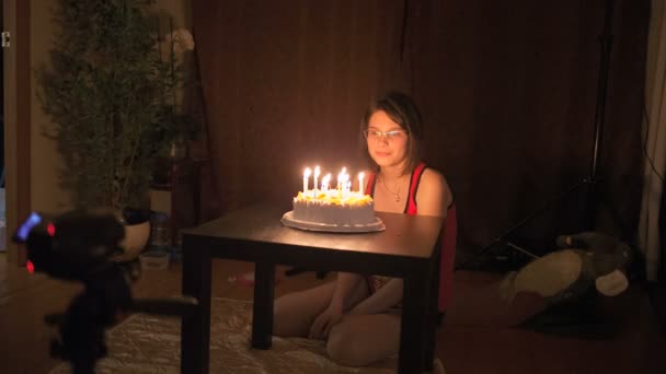 Młoda dziewczyna siedzi przed ciasto ze świecami. — Wideo stockowe