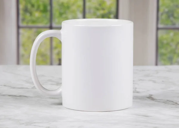 Arka planda pencereleri olan mermer mutfak yüzeyinde fotokopi alanı olan beyaz kahve kupası.