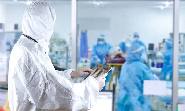 Doctors in the protective suits and masks holding a tablet are examining the corona virus infected patient in the control are