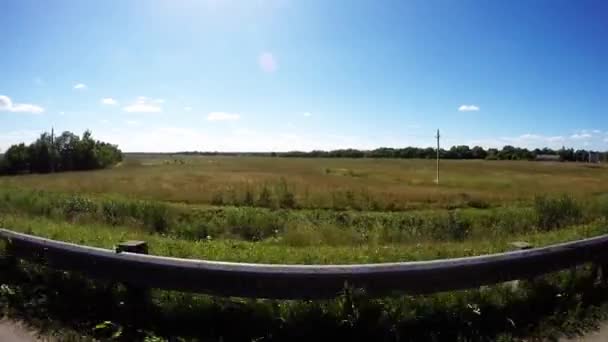 Videocámara entre las ruedas del coche. La cámara vuela sobre la carretera. La cámara flota al margen. Aldea a lo largo de bordillo — Vídeo de stock