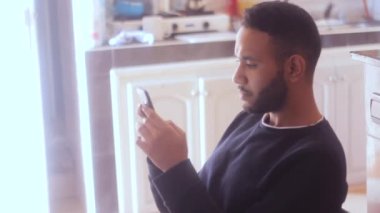  Mutfaktaki cep telefonundan okuyup mesaj yazan endişeli bir adam.