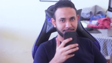 Telefonunu tutan ve kameraya gülümseyen adam.