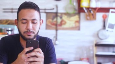 Neşeli sakallı genç adam günlük kıyafetler giyiyor ve sohbet etmek için telefonunu tutuyor.