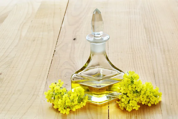 Rapeseed oil with rape flowers over wooden table — Stock Photo, Image