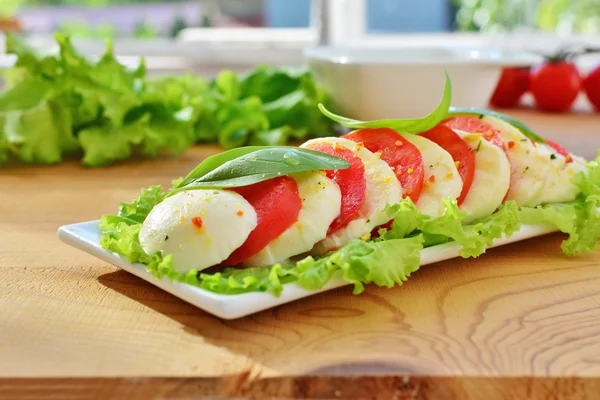 Salada Caprese em prato branco sobre mesa de cozinha de madeira — Fotografia de Stock