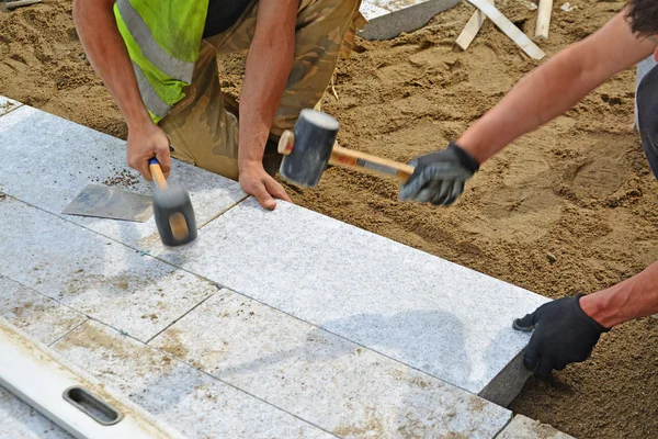 Trabajadores golpeando adoquines en su lugar con mazos de goma . — Foto de Stock