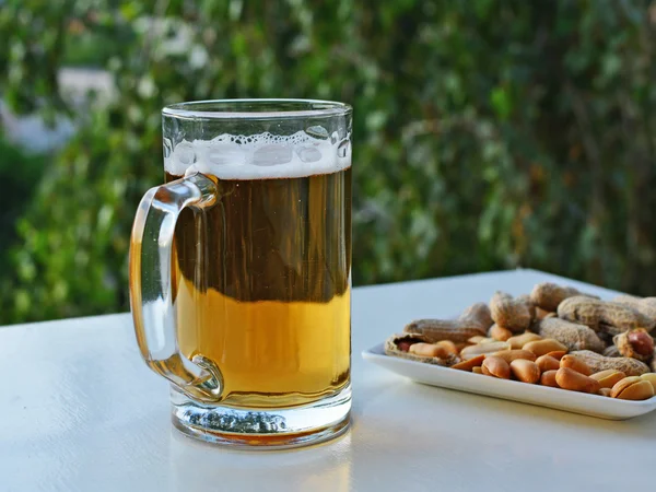 Taza de cerveza ligera y cacahuetes en la mesa — Foto de Stock