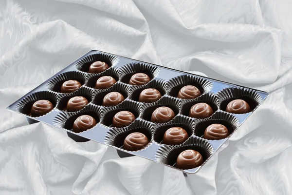 Chocolade snoepjes in bruin vak over zijde achtergrond — Stockfoto