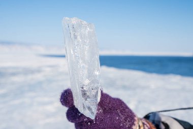 Dişi eller donmuş göl suyunun arka planında bir parça buz tutuyor..