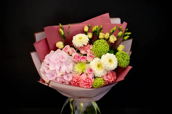A bouquet of fresh flowers in decorative packaging. Photo on a dark background. Congratulatory bouquet.