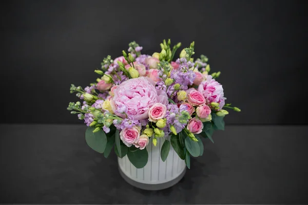 Fresh flowers bouquet with peonies. Assembled in a hat box. Photo on a dark background