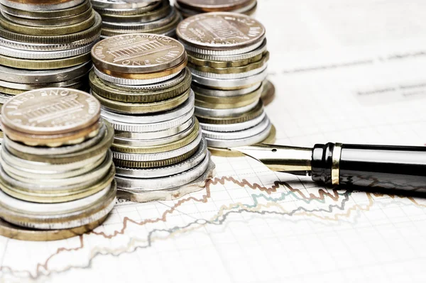 Coins and a fountain pen on charts background — Stock Photo, Image
