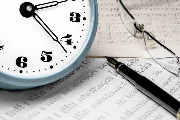 Saat, gözlük ve veri tablosu üzerinde bir dolma kalem