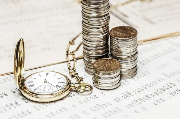 Münzen und eine Uhr auf einem Datentisch — Stockfoto