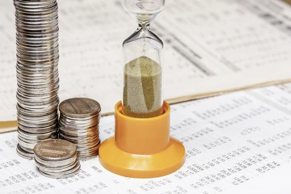 Münzen und ein Sandglas auf einem Datentisch — Stockfoto