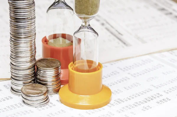 Münzen und ein Sandglas auf einem Datentisch — Stockfoto