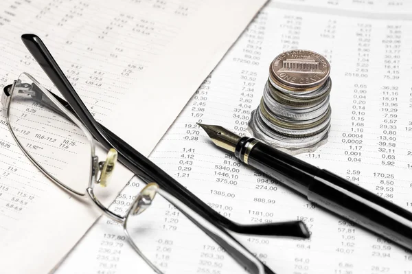 Coins, spectacles and a fountain pen on a data table Royalty Free Stock Photos