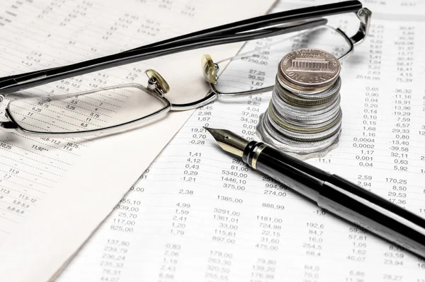Coins, spectacles and a fountain pen on a data table Stock Picture