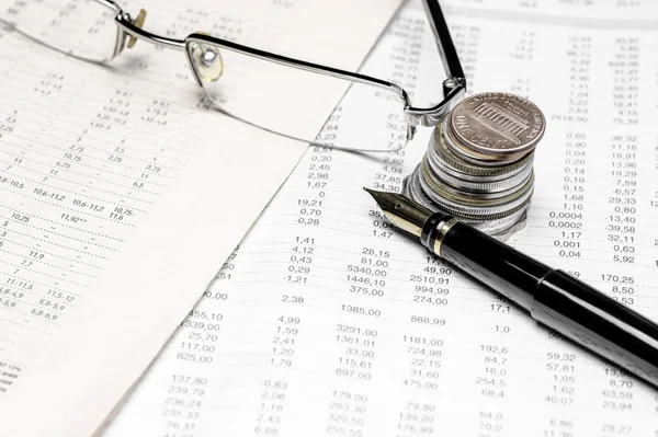 Coins, spectacles and a fountain pen on a data table Stock Image