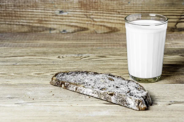 Un bicchiere di latte e del pane su uno sfondo di legno — Foto Stock