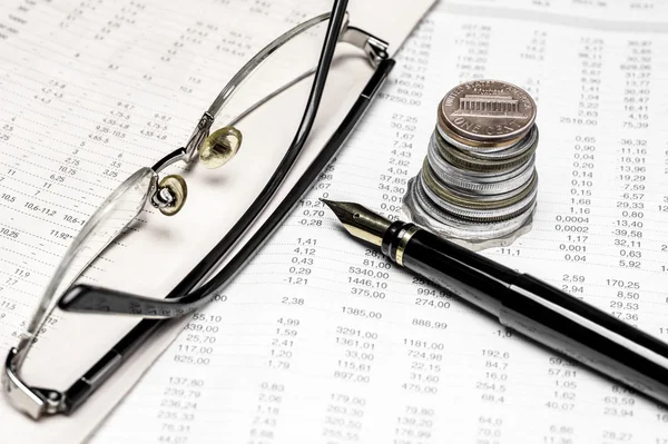 Coins, spectacles and a fountain pen on a data table — Stock Photo, Image