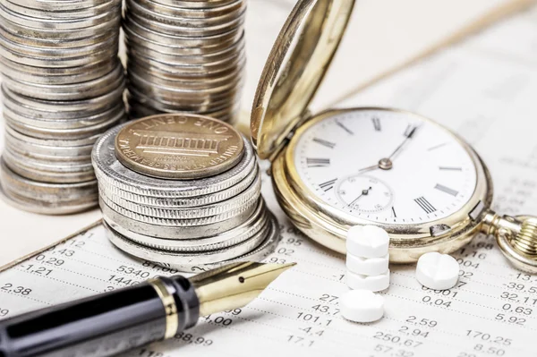 Coins, a clock , a fountain pen and tablets on  a data table — Stock Photo, Image