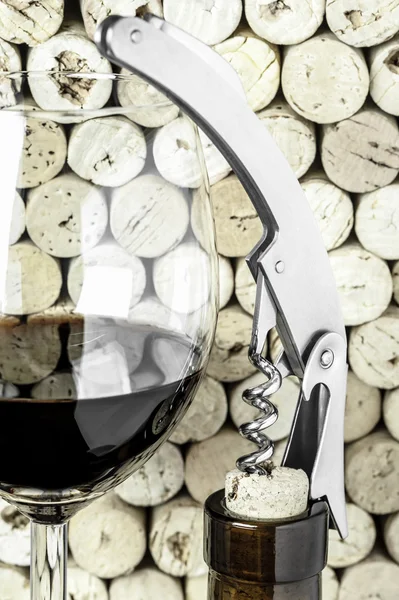 Bir bardak şarap, bir şişe ve bir tirbuşon dikey biçimde mantarlar arka plan üzerinde