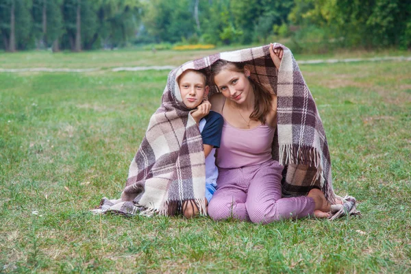 Mladší sestru a bratra stojí pokryté pléd v parku. — Stock fotografie