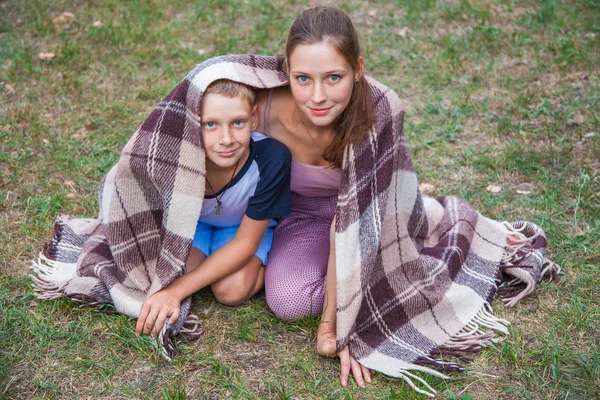 Mladší sestru a bratra stojí pokryté pléd v parku. — Stock fotografie