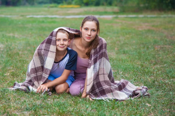 Mladší sestru a bratra stojí pokryté pléd v parku. — Stock fotografie