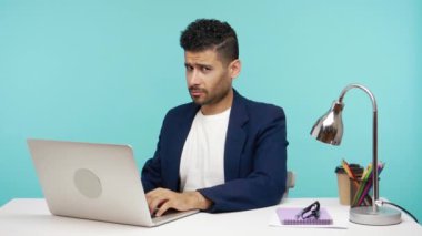 Durdur şunu! İş elbisesi giymiş kızgın bir adam elinde bir avuç dolusu el hareketiyle, ofiste dizüstü bilgisayarla çalışıyor. Mavi arka planda kapalı stüdyo çekimi