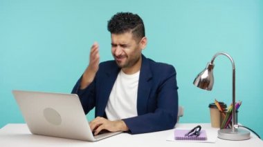 Üzücü üzgün işadamı facepalm jesti yapıyor, tüm parasını kaybediyor, ofiste dizüstü bilgisayarla çalışırken korkunç bir hata yapıyor, iflas ediyor. Mavi arka planda kapalı stüdyo çekimi