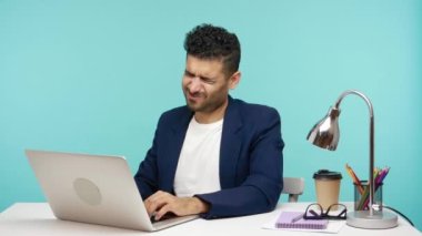 Aşırı çalışan sinirli ofis çalışanı laptopta çalışırken acı veren boyun ve omuzlara masaj yapıyor, yerleşik yaşam tarzı sorunları, osteokondrosis. Mavi arka planda kapalı stüdyo çekimi