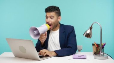 Pozitif ofis çalışanı ofisinde dizüstü bilgisayarının başında otururken yüksek sesle bağırarak reklam, satış ve indirimler yapıyor. Mavi arka planda kapalı stüdyo çekimi