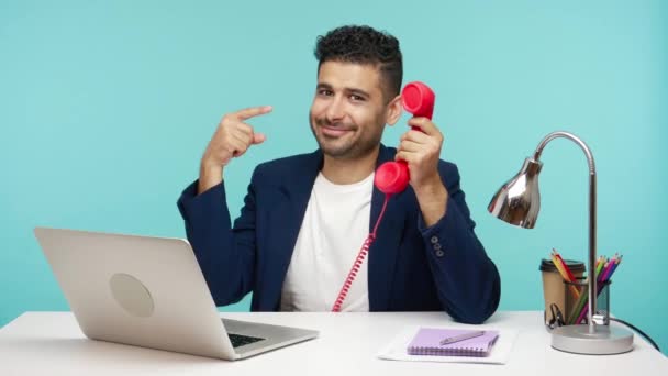 Trabajador Oficina Sonriente Sentado Lugar Trabajo Señalando Con Dedo Teléfono — Vídeo de stock