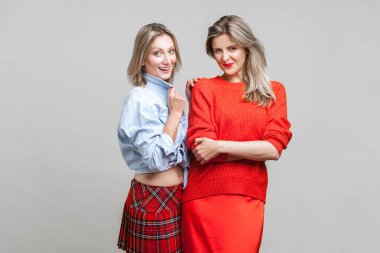 En iyi arkadaşlar. Moda modasına uygun giyinmiş iki kadın modelin birlikte durup kameraya gülümseyişinin portresi. Kadınlar sonbahar trendlerini gösteriyor. Gri arka planda kapalı stüdyo çekimi