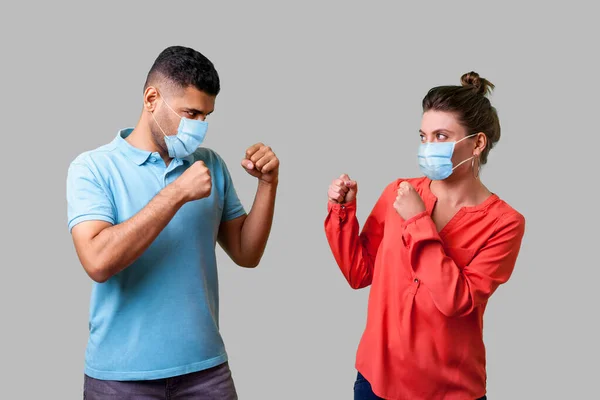 戦いましょう 外科用医療マスクを持つカップルの肖像画が一緒に立って 拳をきれいに保ち 戦うためにお互いを見て 冗談を言います 灰色の背景に隔離され — ストック写真