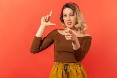 Sen kaybedensin! Kameraya bakıp ezik jesti gösteren sarı saçlı güzel genç bir kadının portresi. Kırmızı arkaplanda kapalı stüdyo çekimleri.
