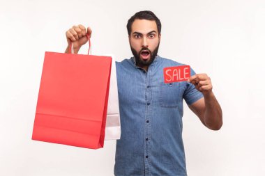 Satış kartı ve alışveriş çantalarını tutan ve gösteren heyecanlı bir adam. Büyük final satışıyla şok olmuş, Kara Cuma. Beyaz arka planda izole edilmiş kapalı stüdyo görüntüleri